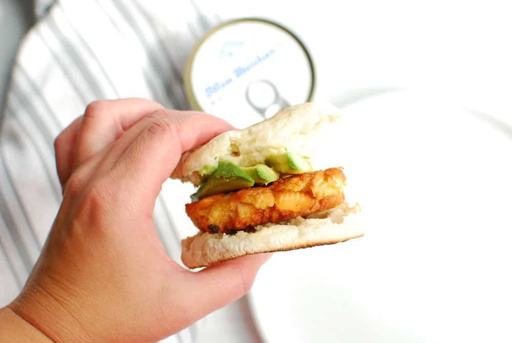 a woman's hand holding a salmon patty breakfast sandwich