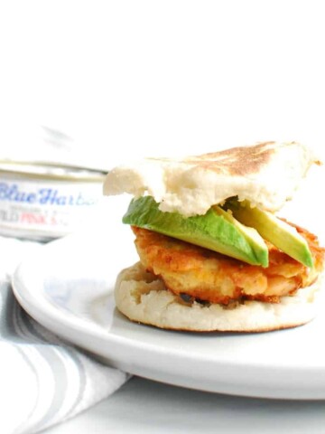 A salmon breakfast sandwich with avocado on a white plate.
