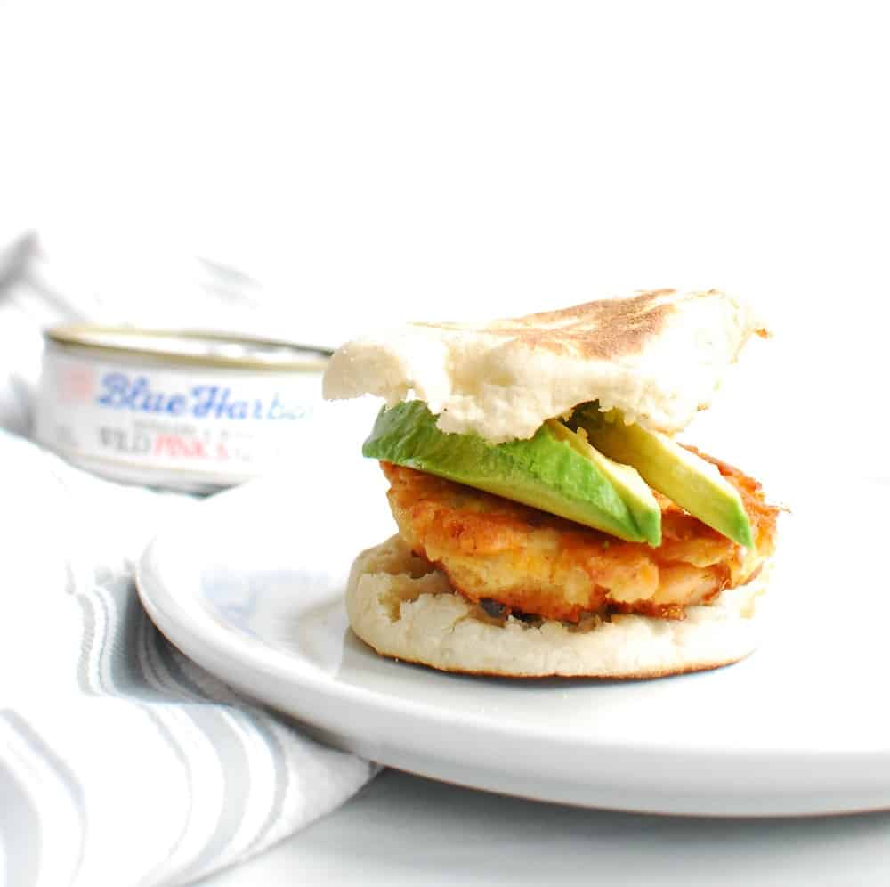 A salmon breakfast sandwich with avocado on a white plate.