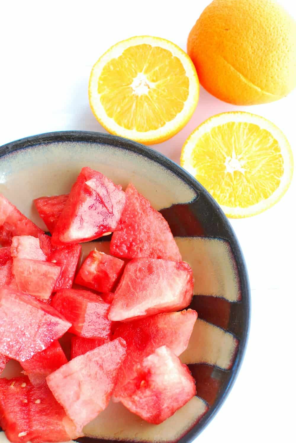 chopped watermelon in a bowl next to some sliced oranges