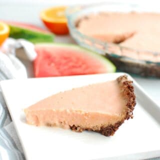 a slice of watermelon pie on a white plate next to a napkin and some extra watermelon