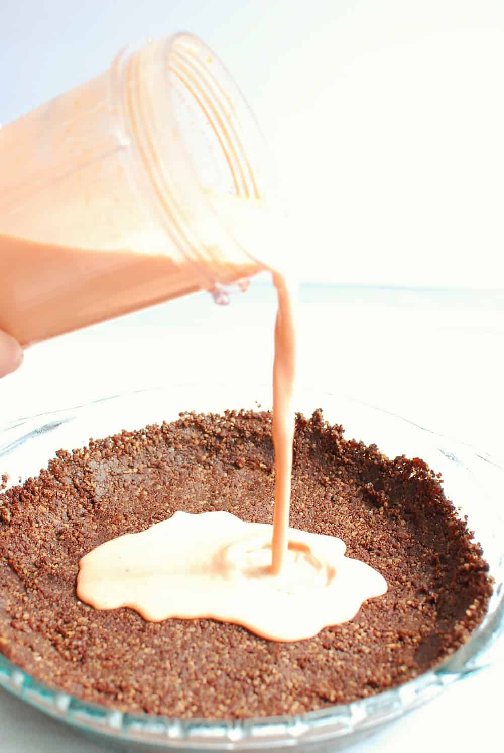 a woman pouring a watermelon citrus filling into a prepared nut-based pie crust