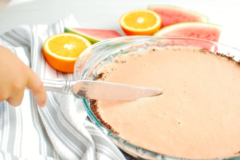 a hand holding a knife cutting into a watermelon pie