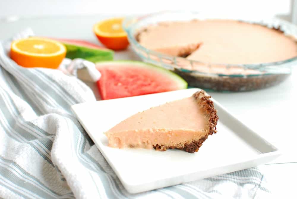 a slice of watermelon freezer pie on a plate next to a napkin, some sliced oranges, and some watermelon