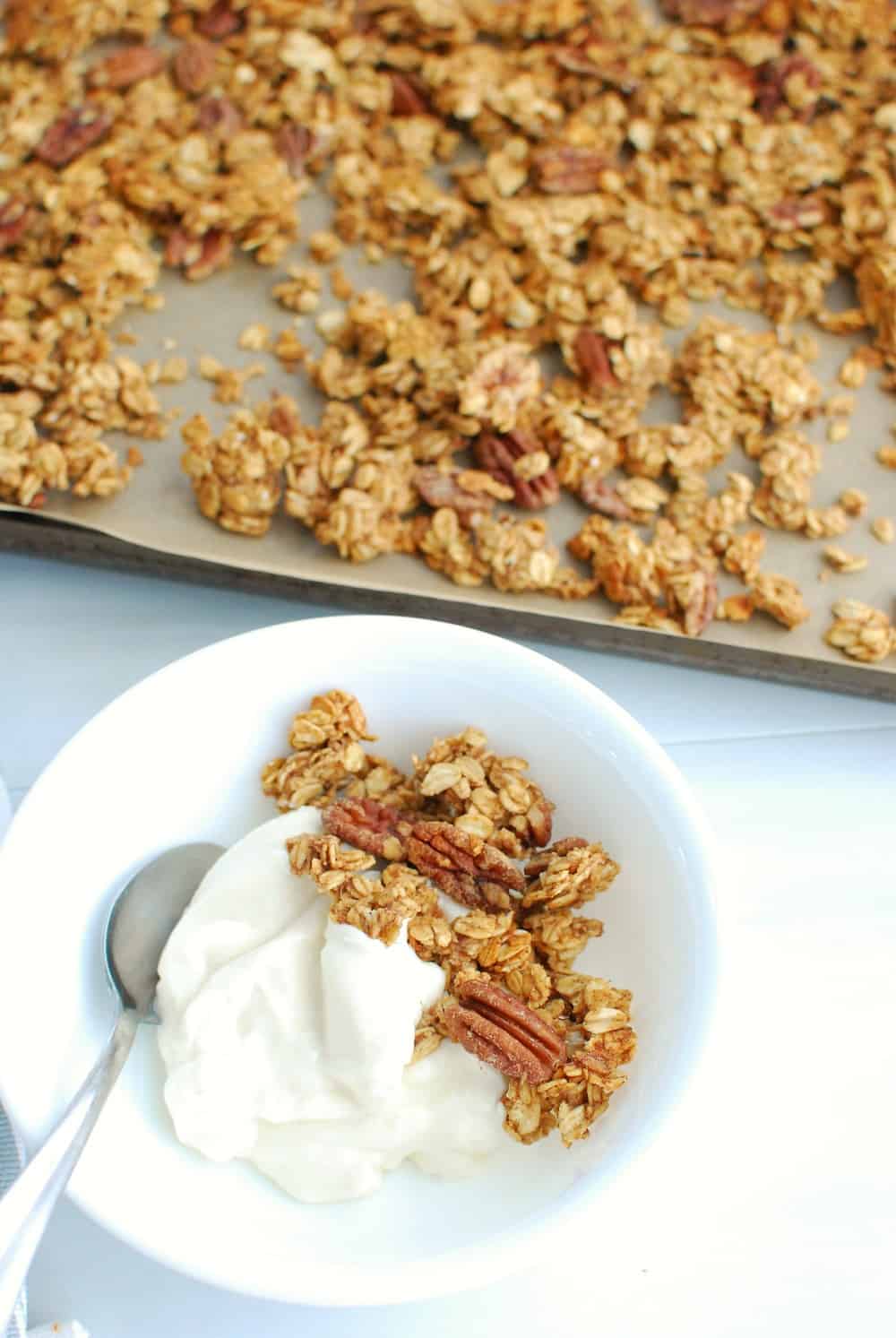 a bowl of yogurt with peanut butter banana granola on top, and the baking sheet of granola next to it