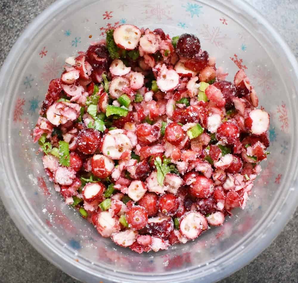 Cranberries mixed in a bowl with jalapeno, lime, sugar, salt, cilantro and scallions.