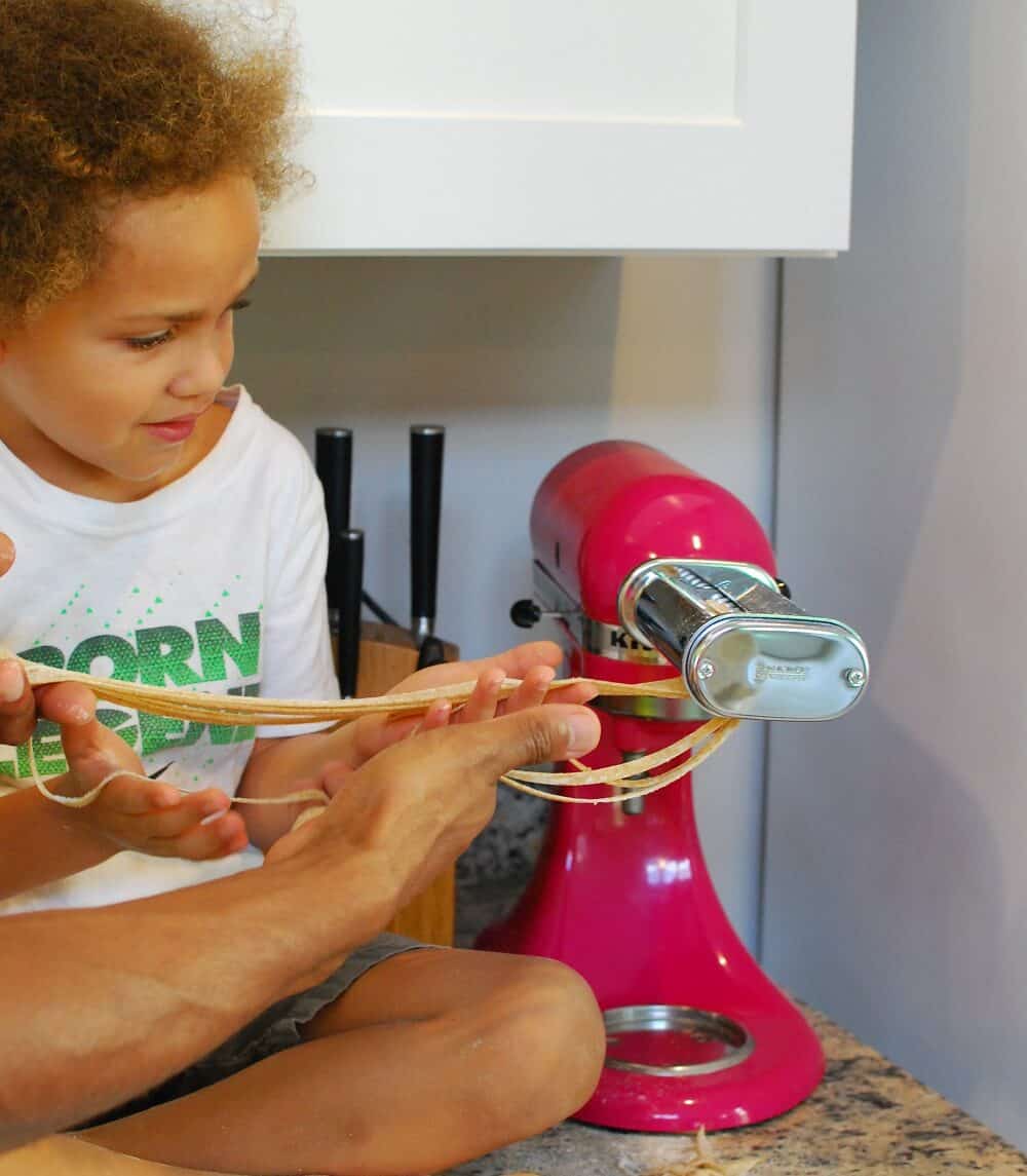 a little boy making fettuccine noodles with a stand mixer attachment