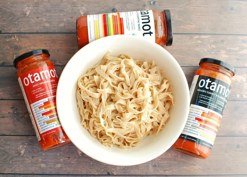 several jars of tomato sauce around a bowl of cooked pasta