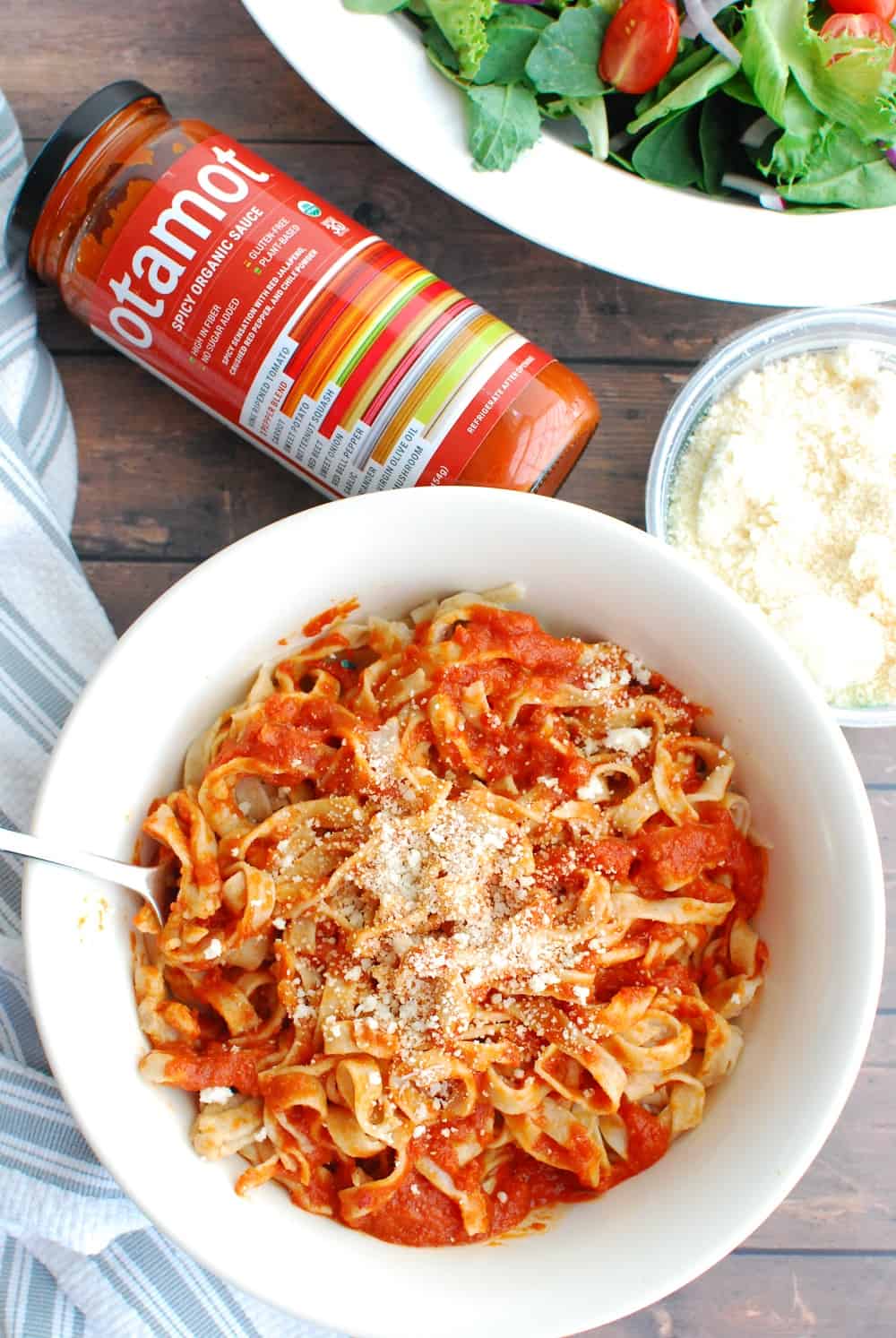 a bowl of cooked sourdough pasta tossed with sauce next to a jar of sauce and a bowl of salad