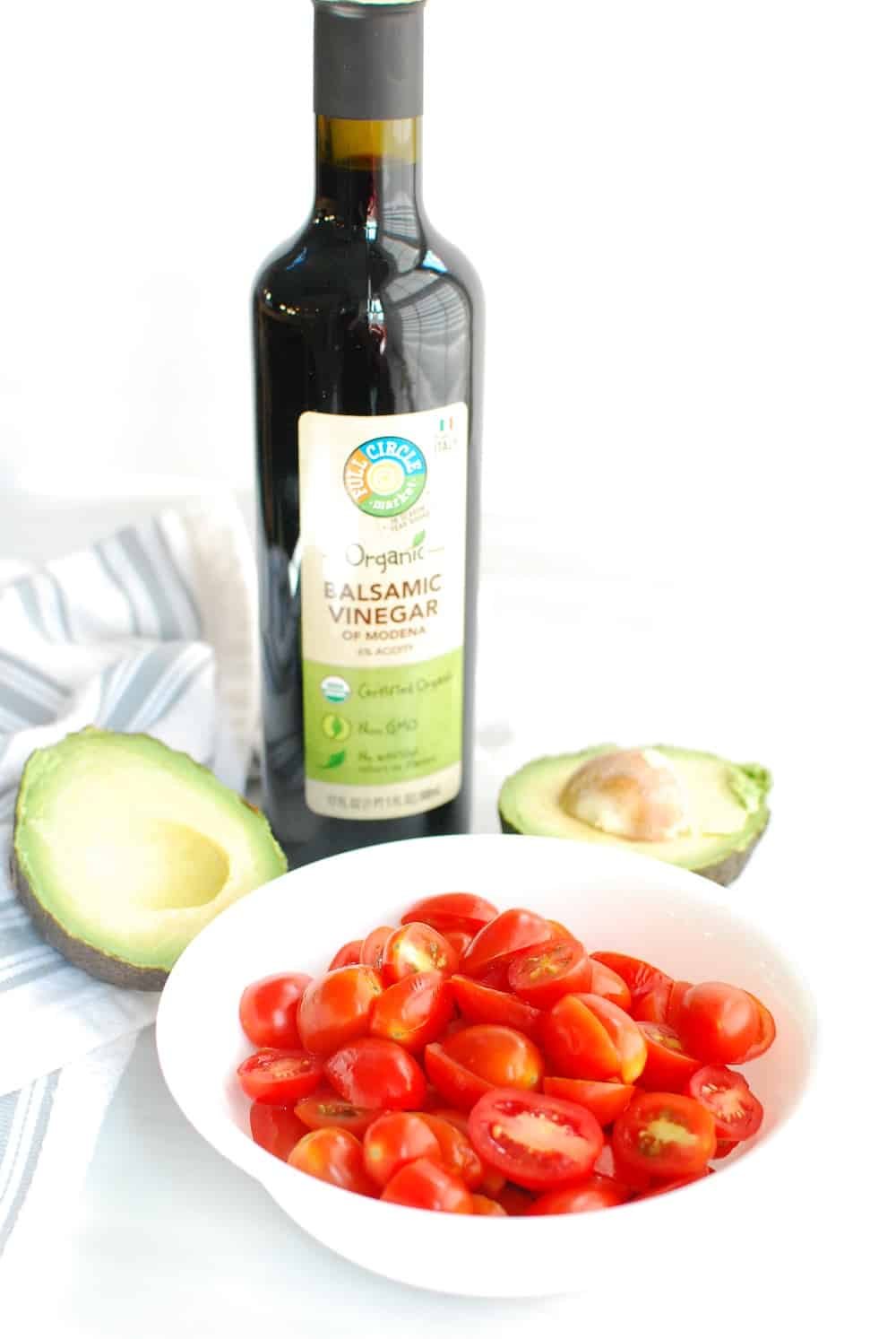 a bottle of balsamic vinegar next to a bowl of cherry tomatoes and a halved avocado