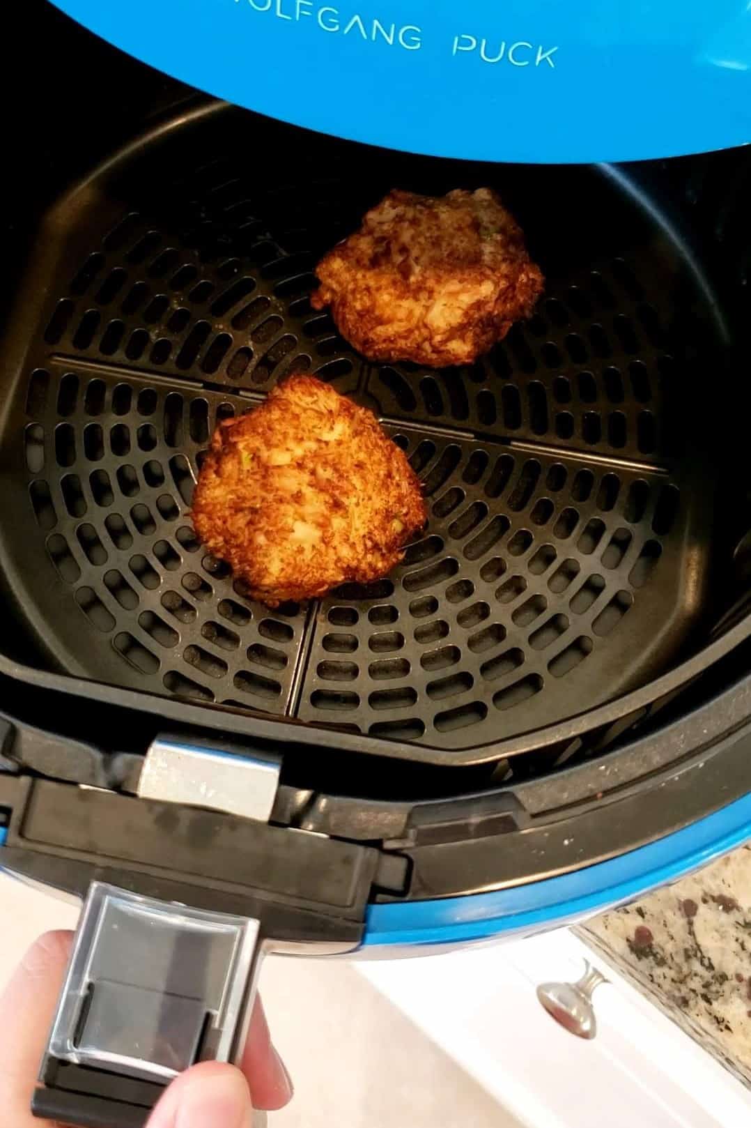 two salmon patties in an air fryer basket after just finishing cooking