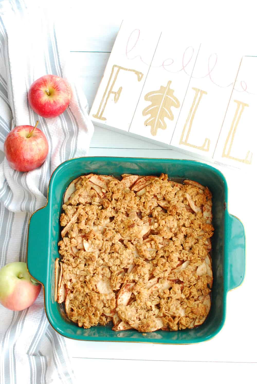 a baking dish full of honey apple crisp, next to a few apples and a flal 