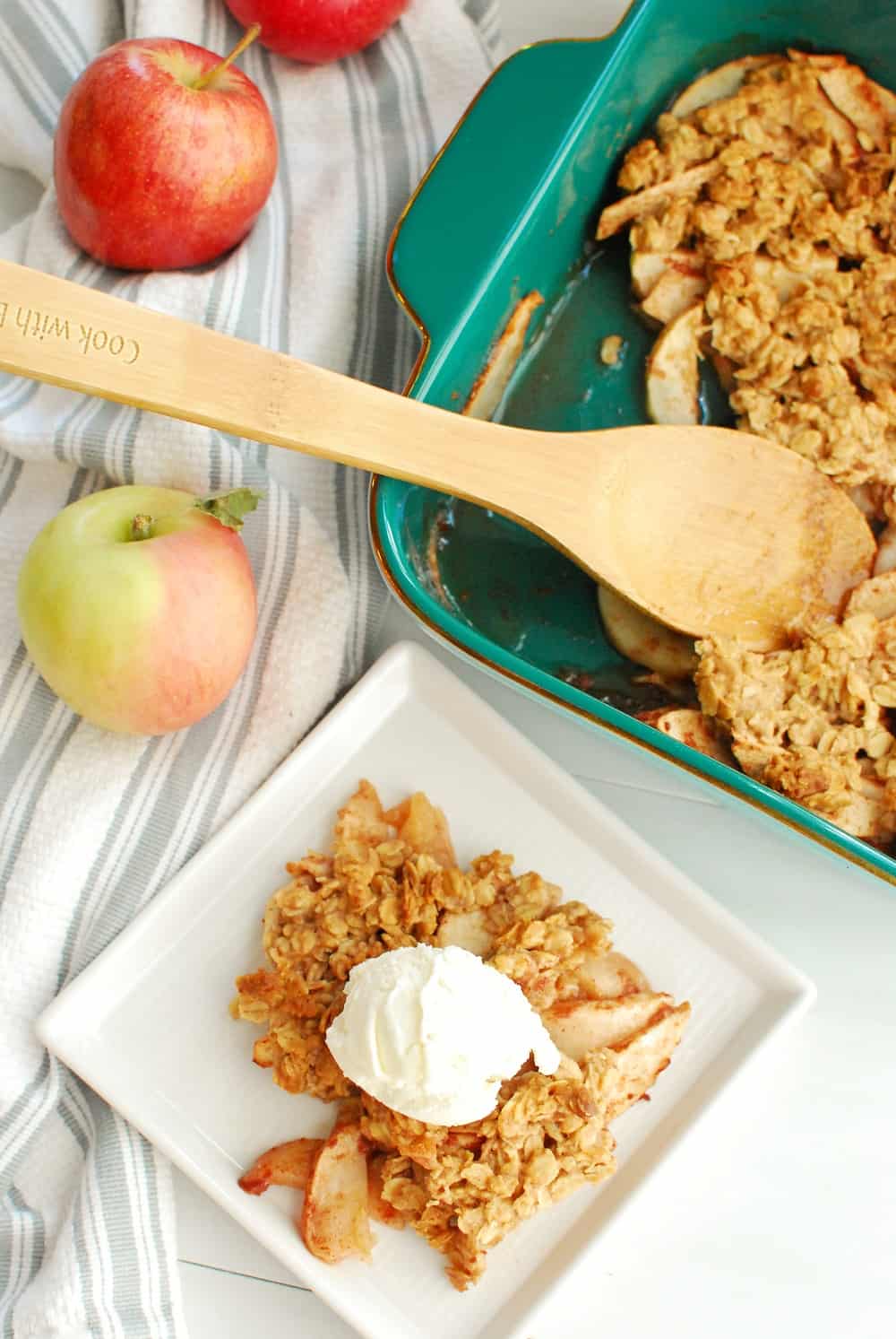 a scoop of honey apple crisp on a white plate with a scoop of ice cream, next to a baking dish of apple crisp