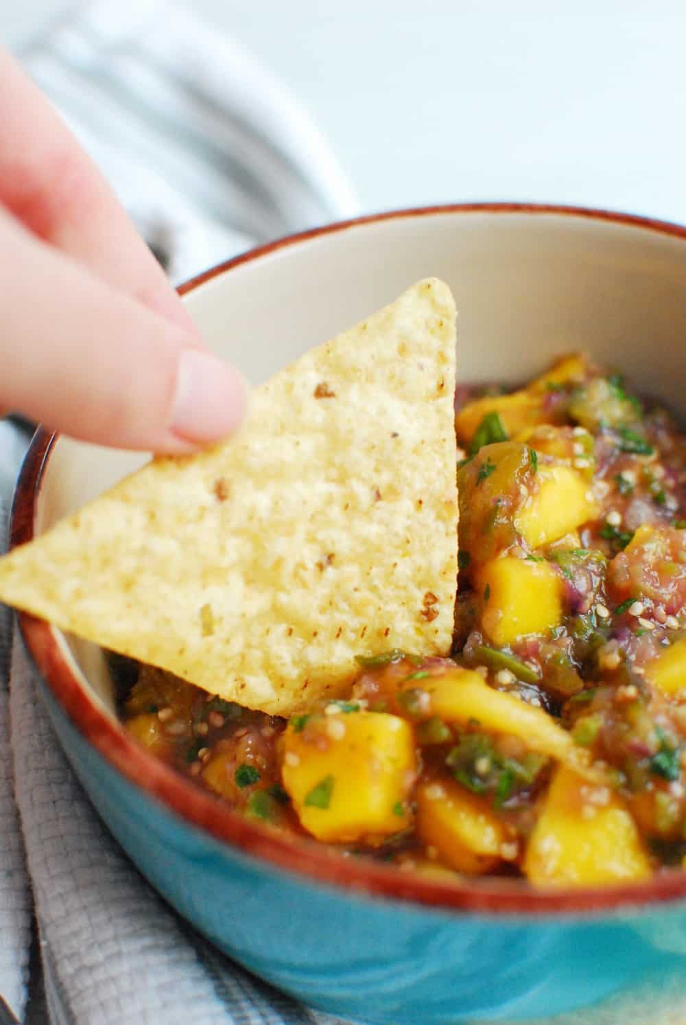 a person's hand dipping a chip in salsa