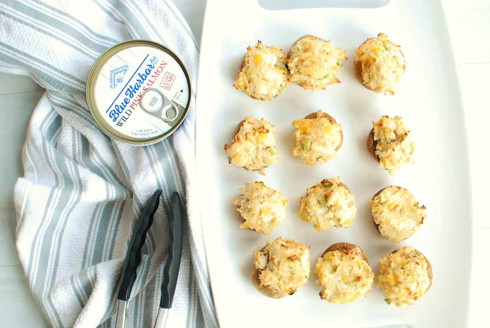 overhead shot of 12 salmon stuffed mushrooms next to a can of salmon and some tongs