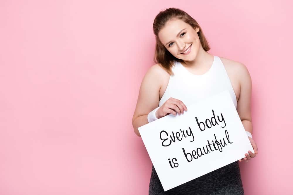 a woman holding a sign that says every body is beautiful