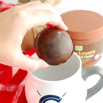 A woman holding a hot chocolate bomb about to put it in a coffee mug.
