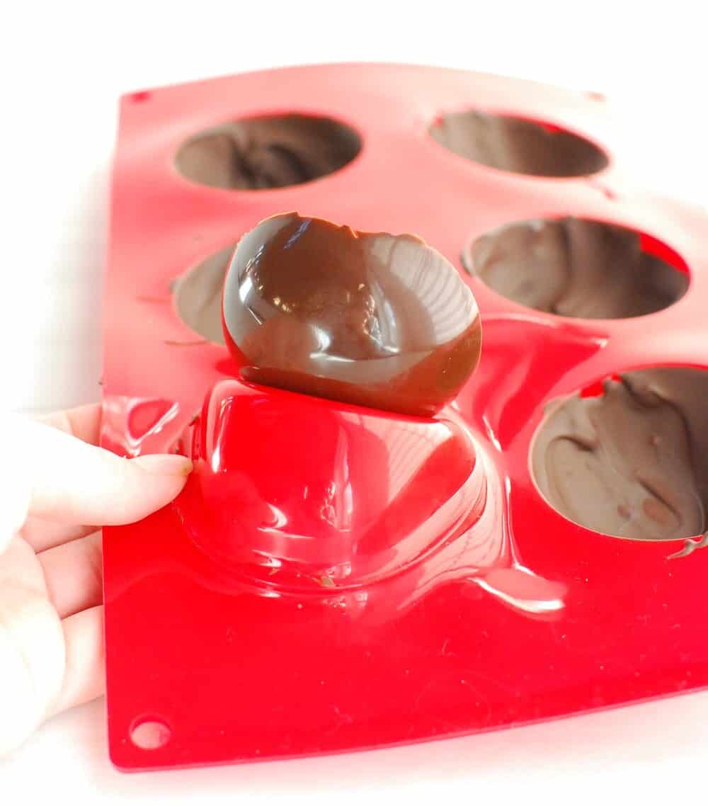 a woman's hand popping a chocolate dome out of the silicone mold