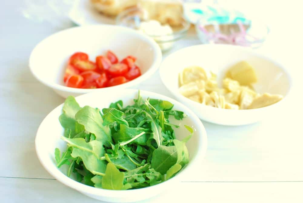 three small bowls, one with arugula, one with tomatoes, and one with artichokes