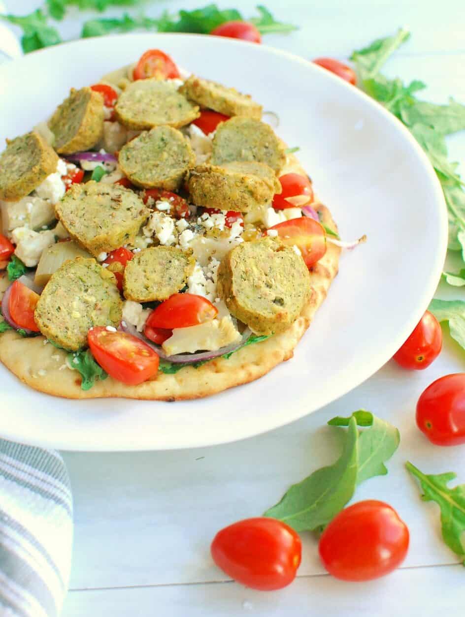 a flatbread on a white plate next to arugula and cherry tomatoes