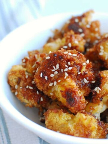 a bowl full of teriyaki cauliflower next to a striped napkin