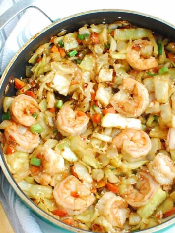 A sauté pan filled with shrimp egg roll in a bowl next to a wooden spoon.