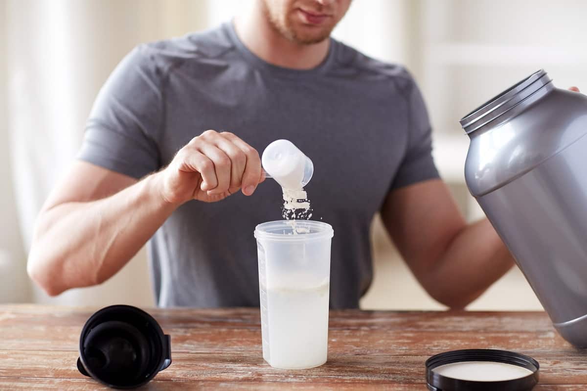 a man putting whey protein powder into a shaker bottle