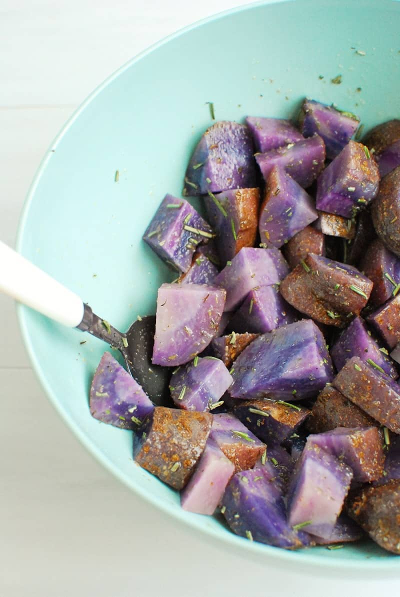 A mixing bowl where purple potatoes are mixed with oil and seasonings.