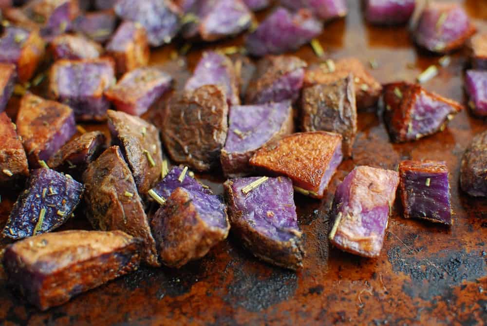 Roasted purple potatoes on a baking sheet right after coming out of the oven.