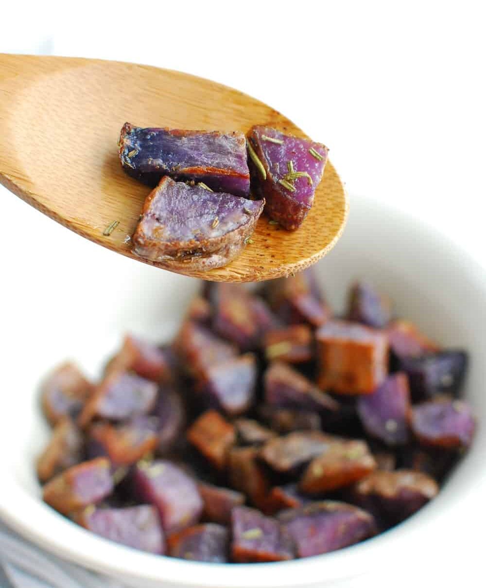 A wooden spoon with three roasted purple potatoes on it.