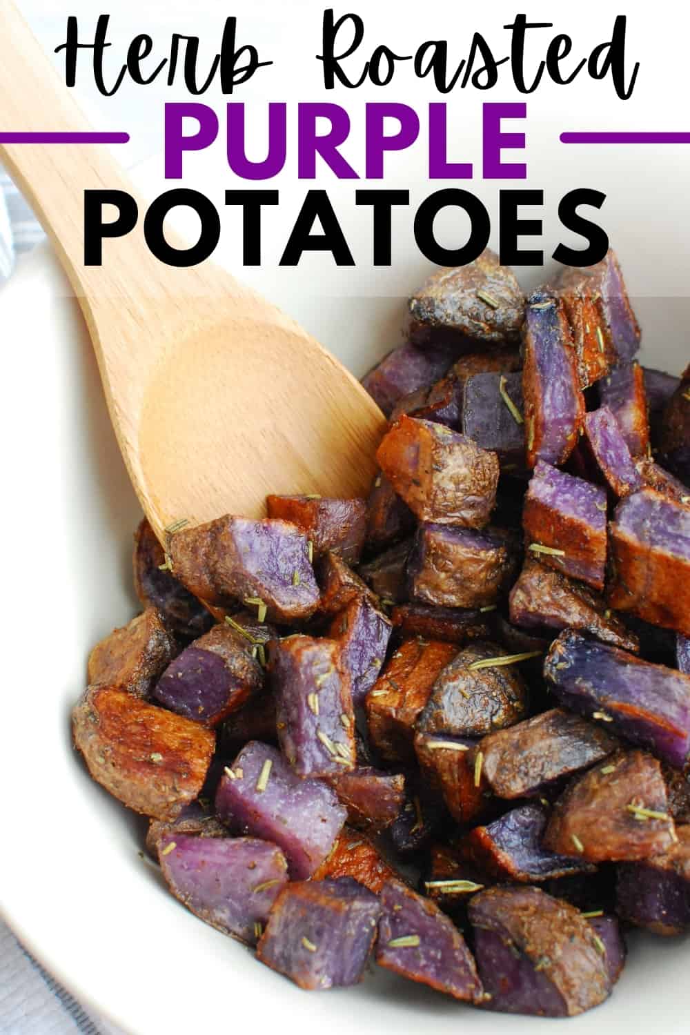 A bowl full of herb roasted purple potatoes with a wooden spoon in the bowl.