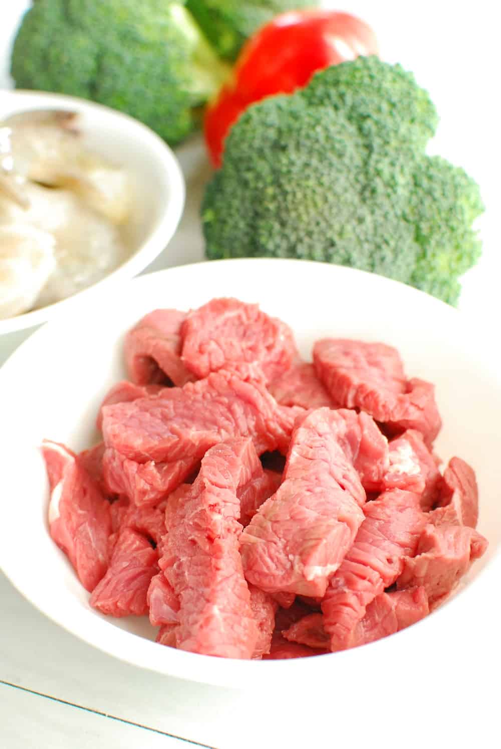 Steak in a bowl next to broccoli and shrimp.
