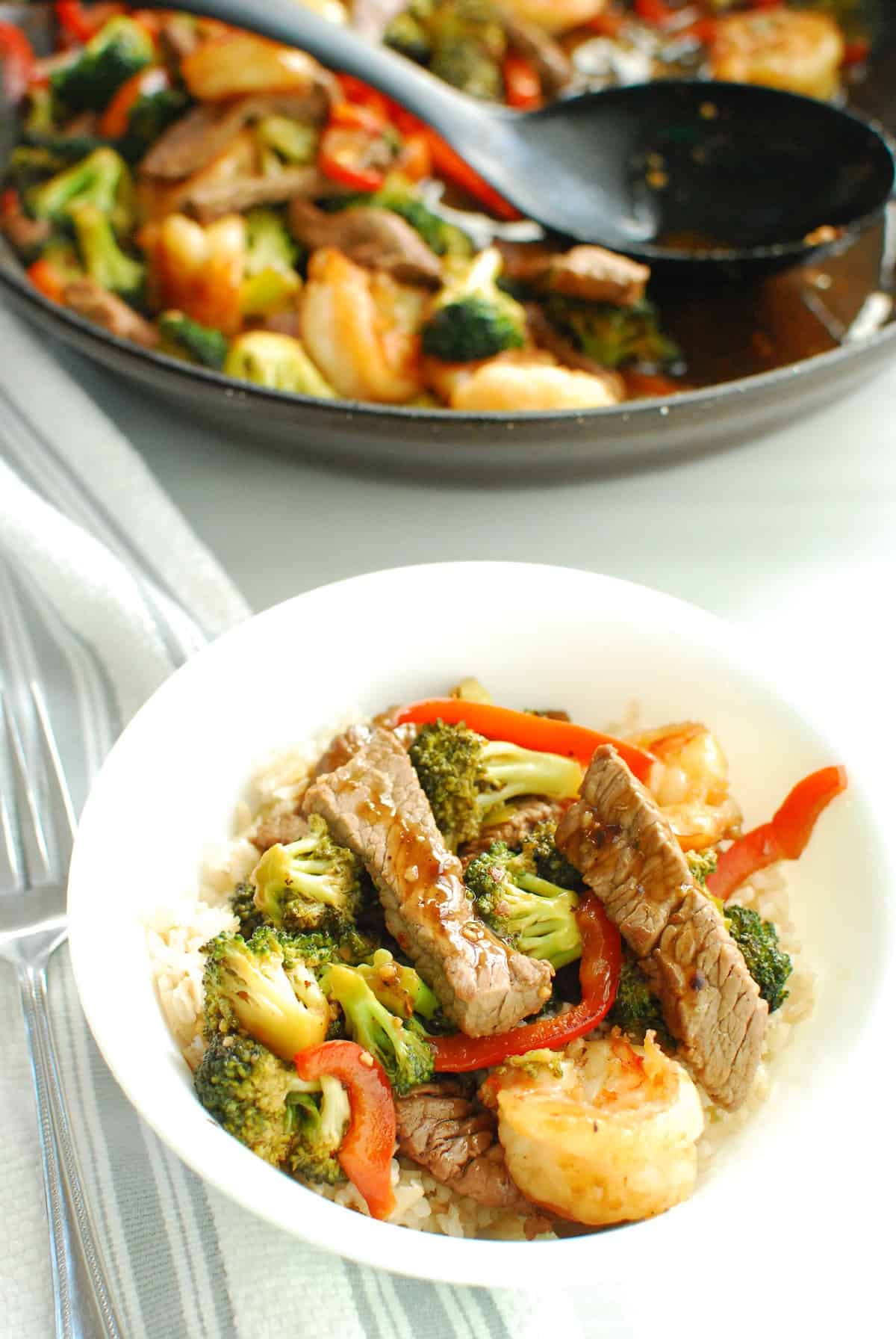 A bowl of stir fry next to a skillet with stir fry.