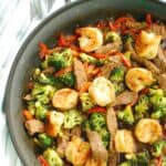 A close-up of a skillet full of steak and shrimp stir fry.