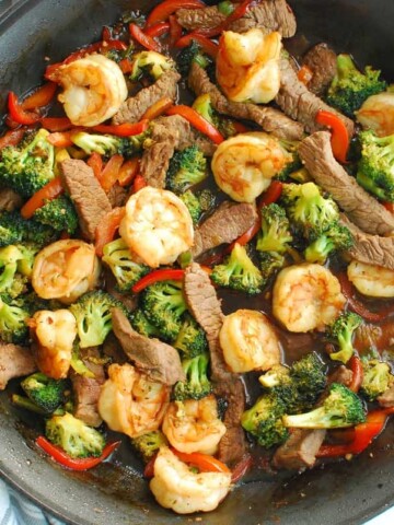 A skillet of shrimp and steak stir fry next to a striped napkin.