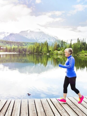 An older female running outside on a bridge crossing a pond.