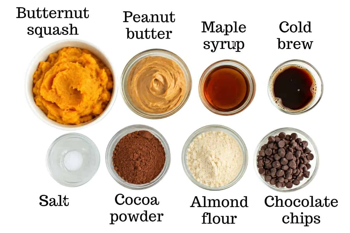 Butternut squash, peanut butter, maple syrup, cold brew, salt, cocoa powder, almond flour, and chocolate chips on a white backdrop.