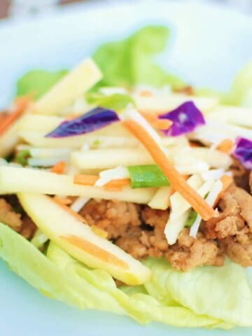 A hoisin ground turkey lettuce wrap on a white plate on top of a brown napkin.