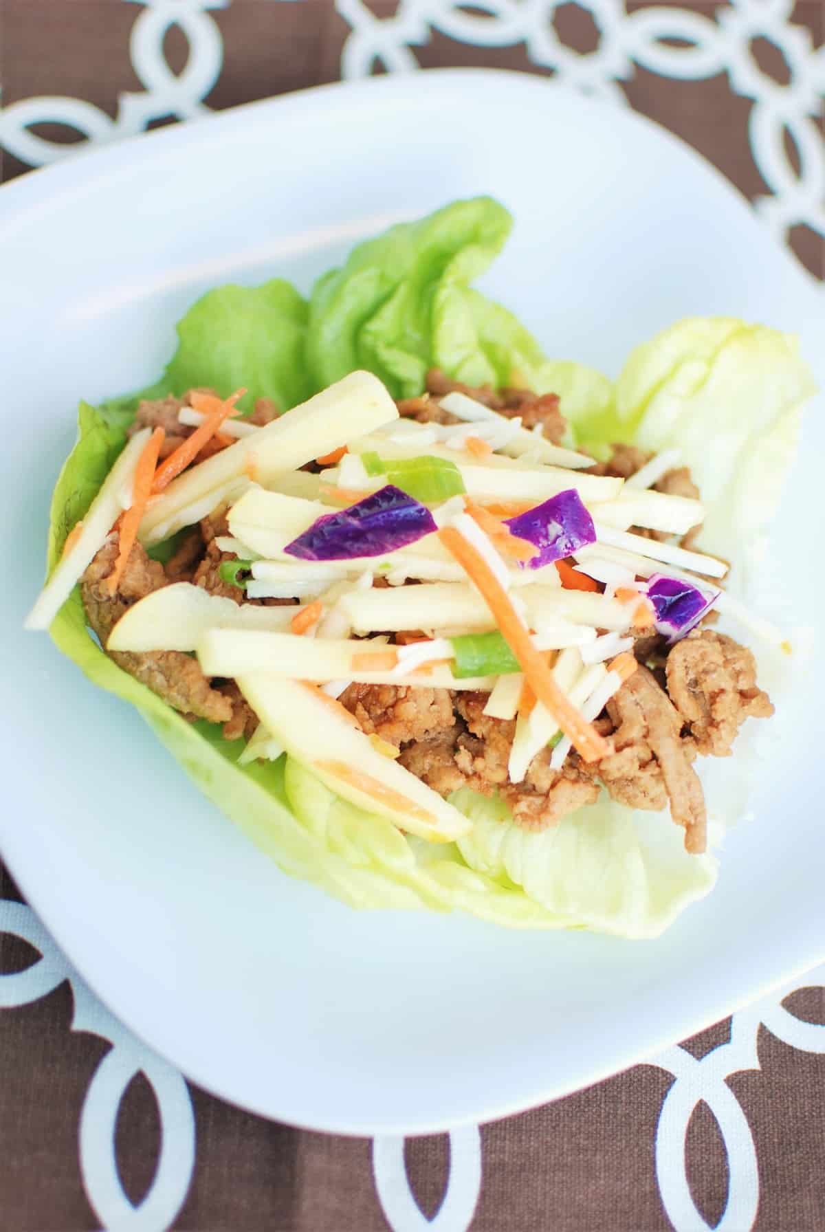 A lettuce wrap filled with hoisin ground turkey and cabbage apple slaw, on a plate, next to a brown napkin.