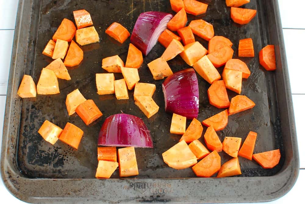 A baking sheet with chopped carrots and sweet potatoes, and a quartered red onion.