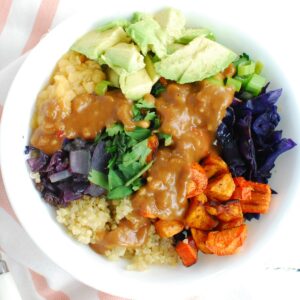 A quinoa lentil bowl with veggies topped with peanut sauce, next to a white and pink napkin.