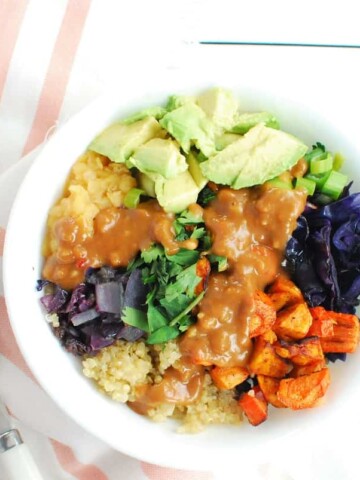 A lentil quinoa bowl with lots of veggies and peanut sauce on top.
