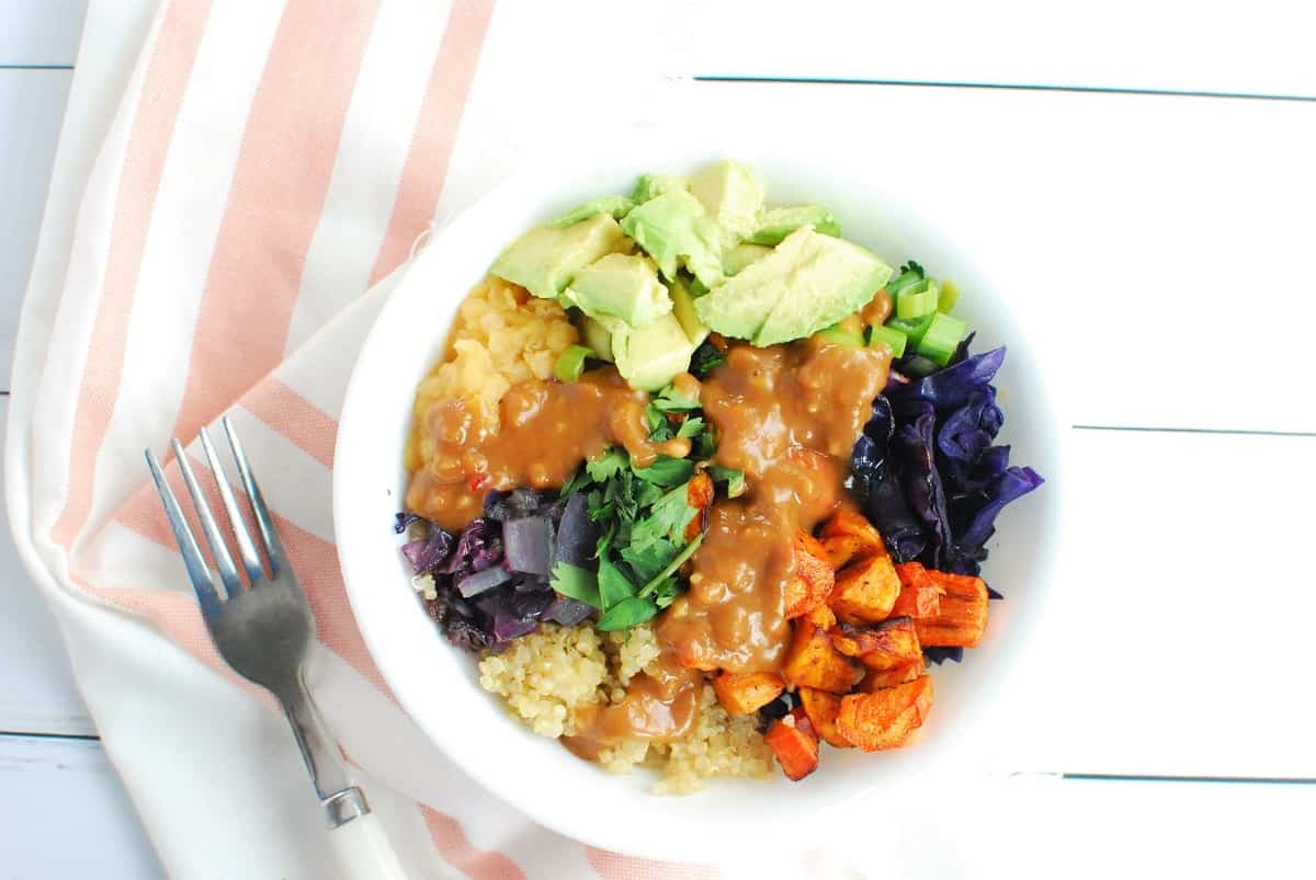 A lentil quinoa bowl with lots of veggies and peanut sauce on top.
