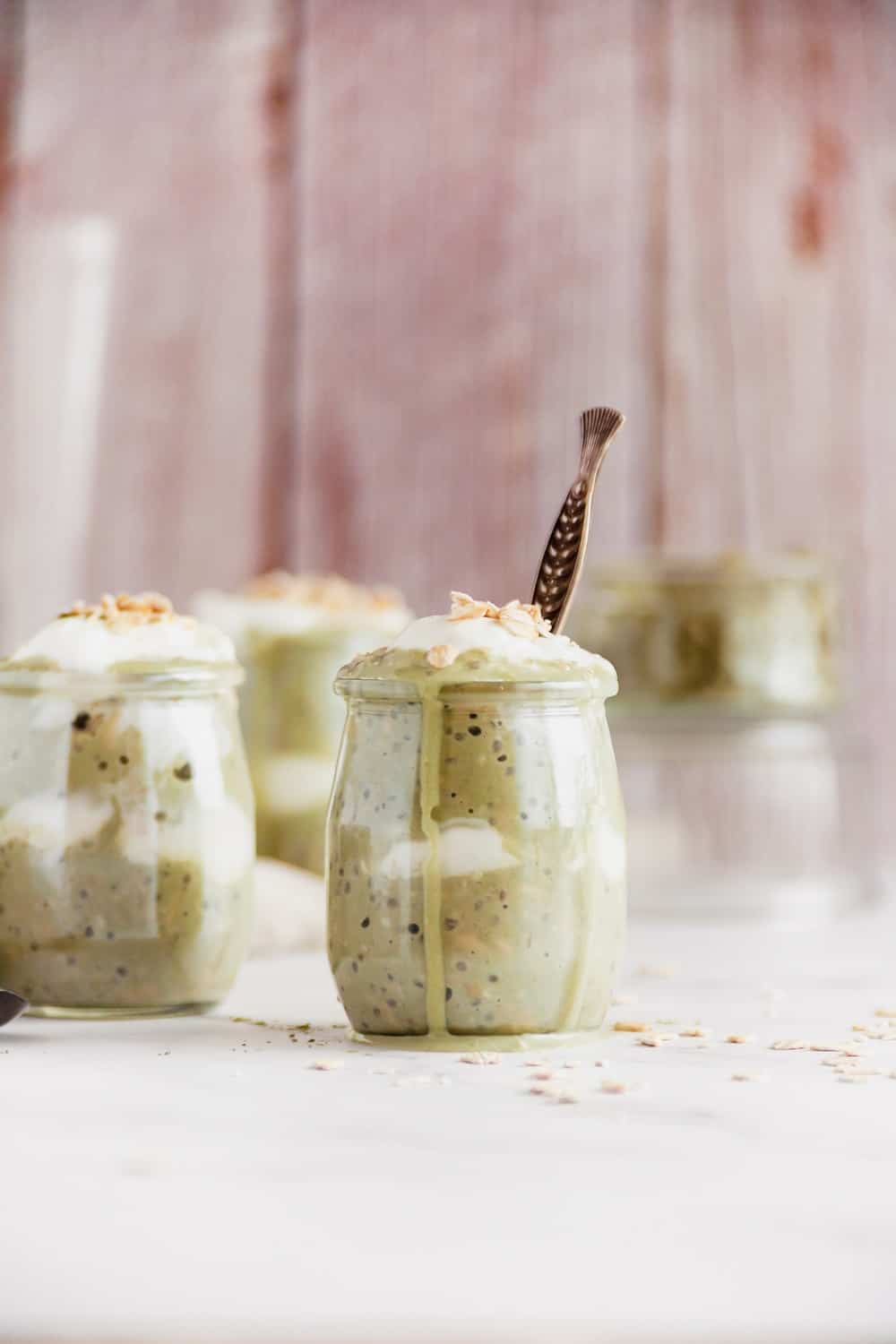 A glass jar of matcha overnight oats with a little spilling out over the edge.