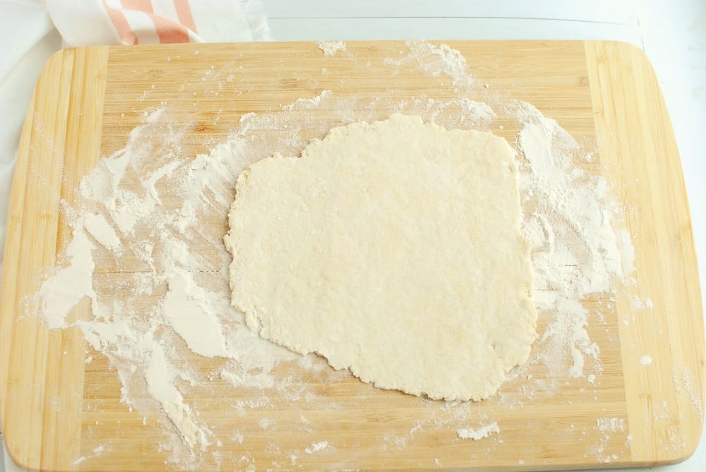 Pizza dough that's been rolled out flat on a wooden board.