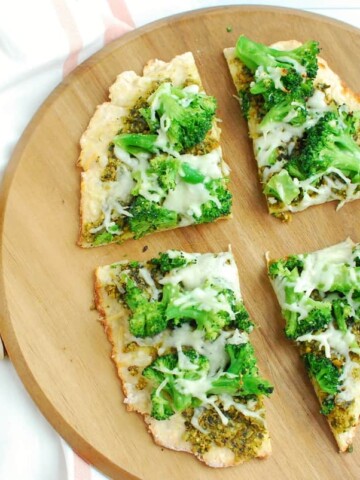 Four slices of pistachio pesto pizza on a cutting board, next to some scattared in-shell pistachios.