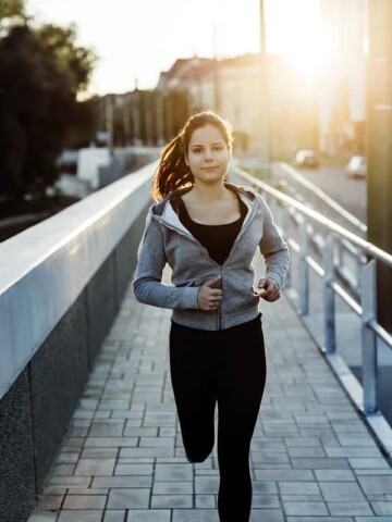 A woman running on the sidewalk, training for a 10K.