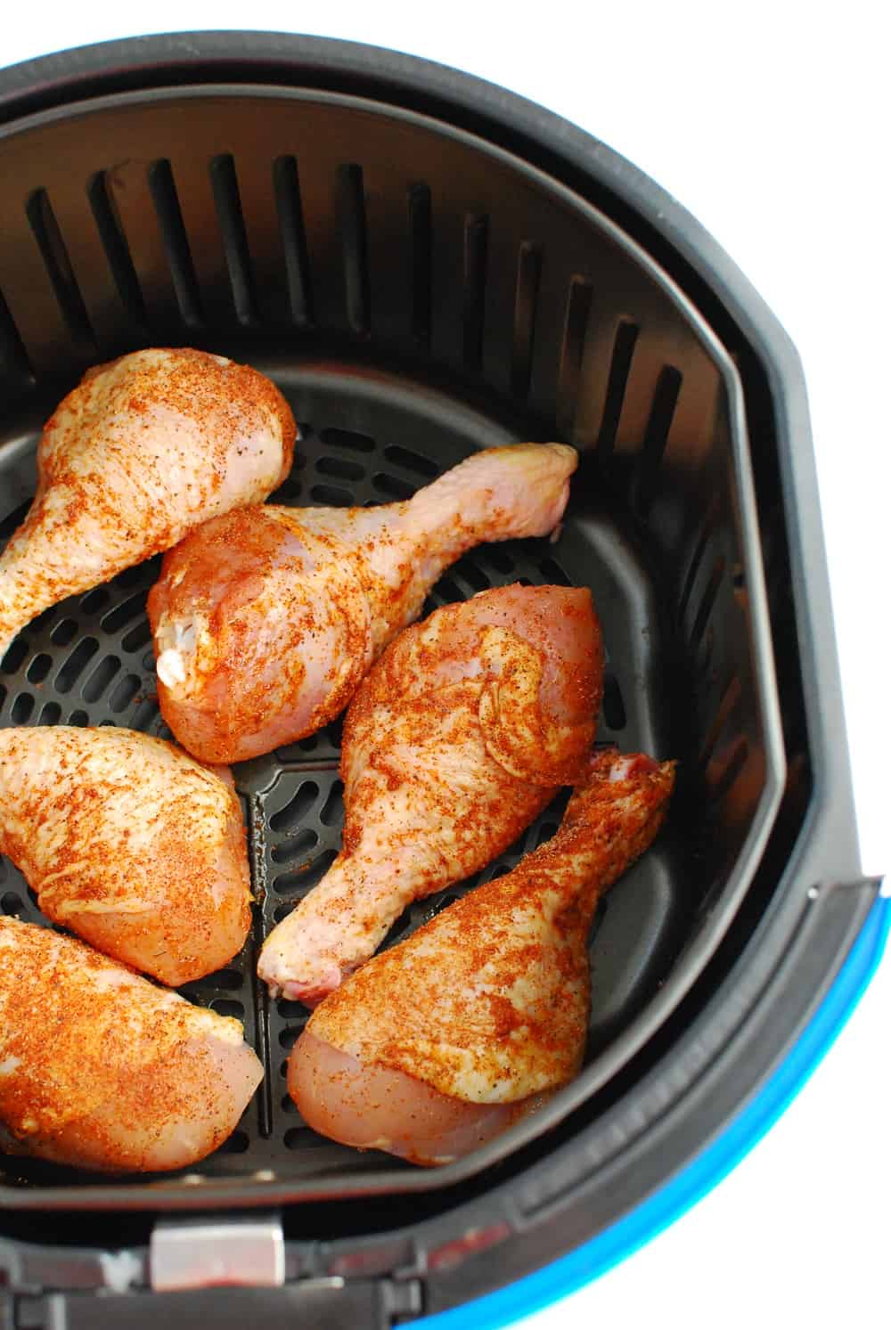 Uncooked chicken drumsticks in the basket of the air fryer.