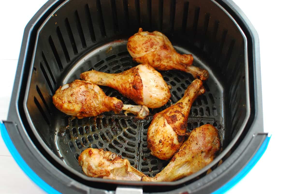 Cooked chicken drumsticks in the basket of an air fryer.