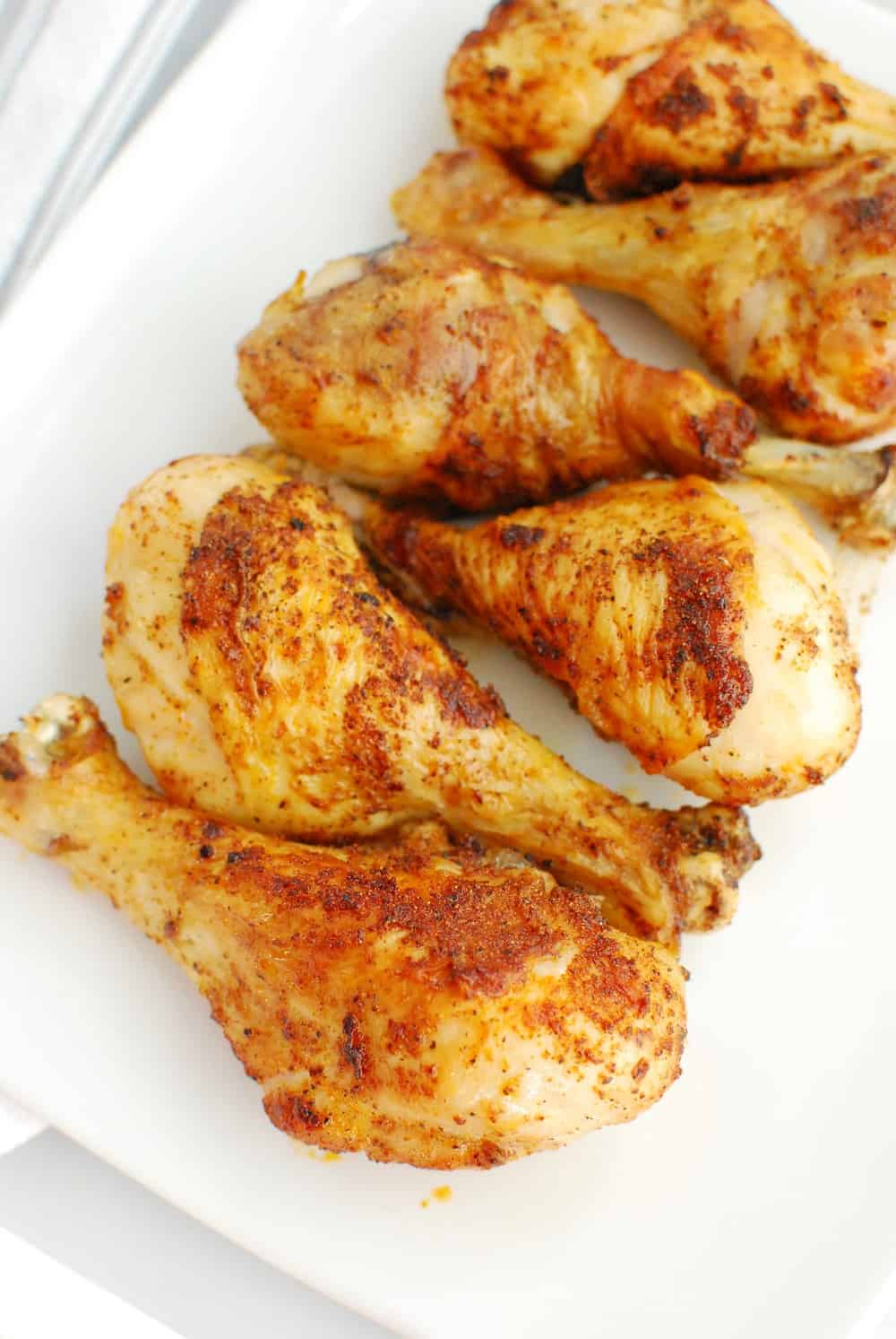 A close up of several air fryer chicken drumsticks on a white plate.